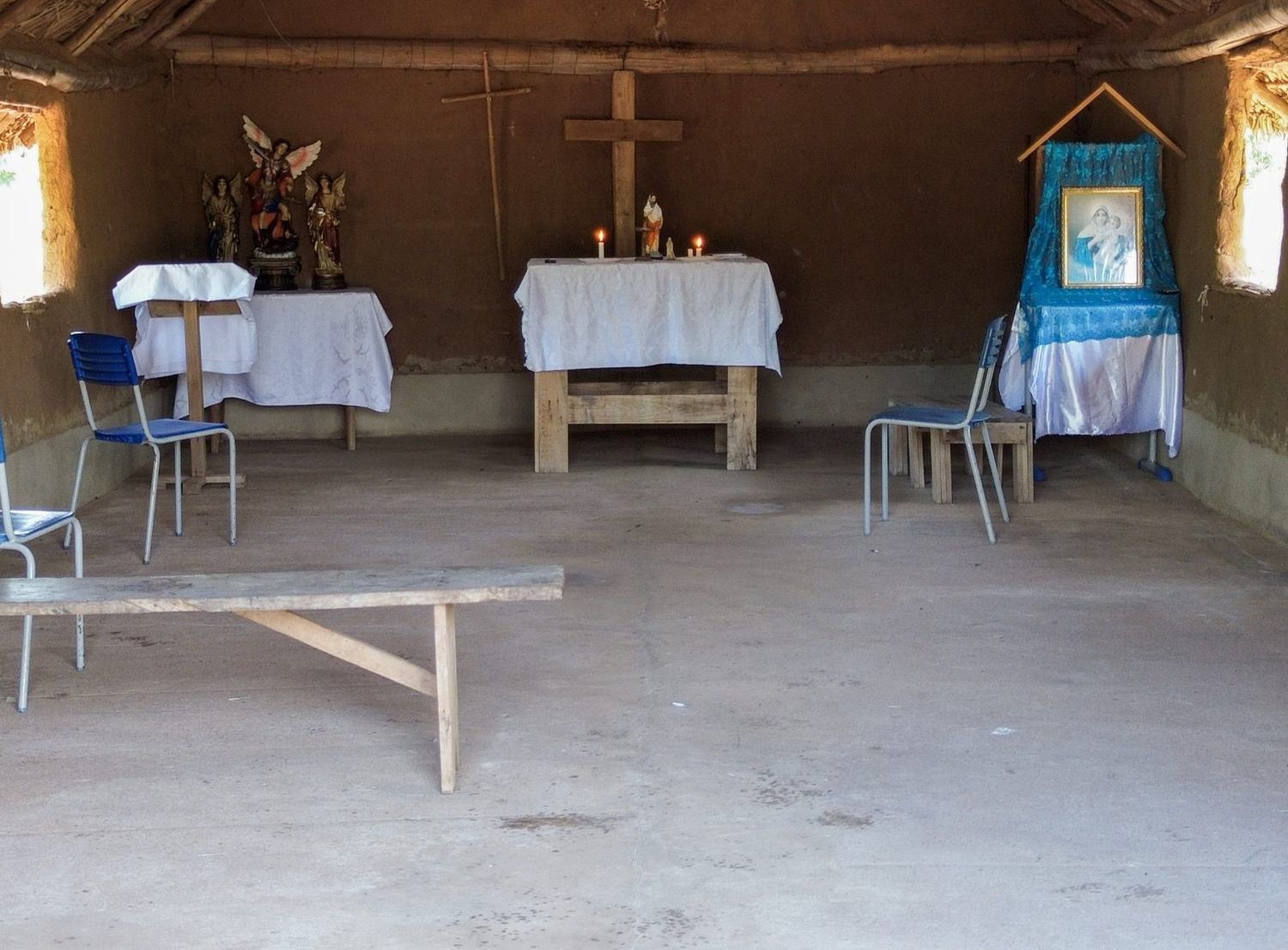 Interior da capela da aldeia, com altar, imagens de santos e cruz de madeira