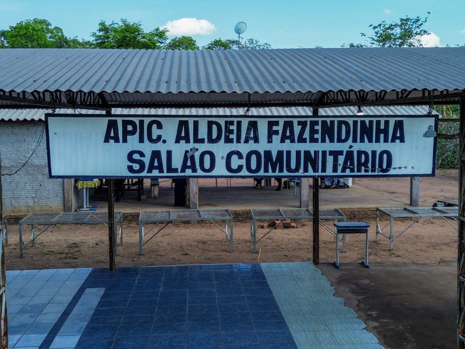 Placa do salão comunitário da APIC, Aldeia Fazendinha, com as mesas da feira montadas