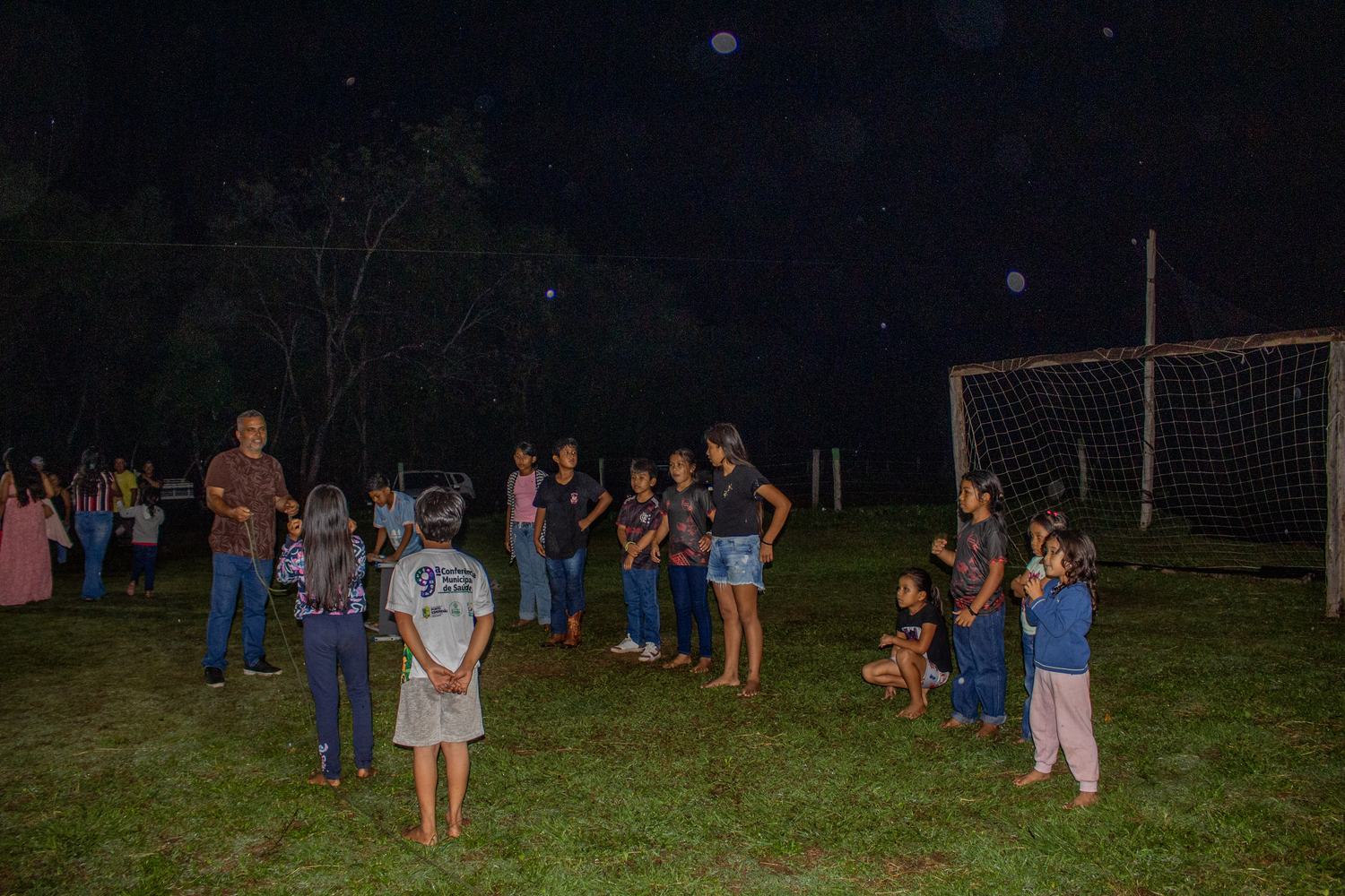 Crianças da aldeia reunidas no campo, à noite, durante as brincadeiras da noite cultural