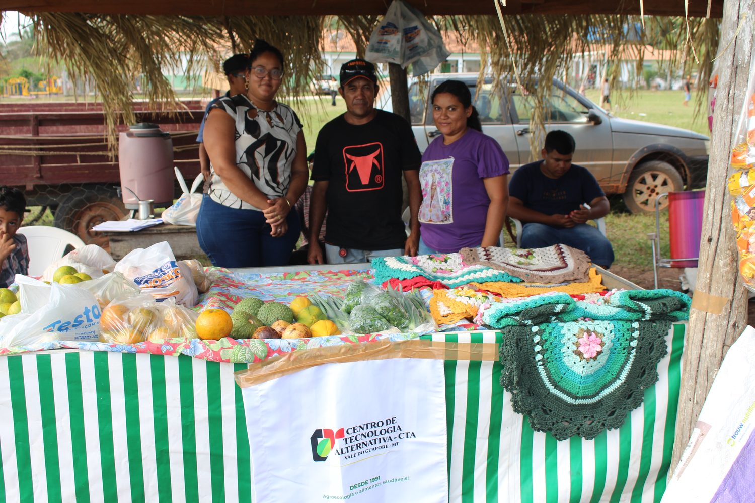 Famílias atrás da banca com frutas, crochê e produtos dos quintais