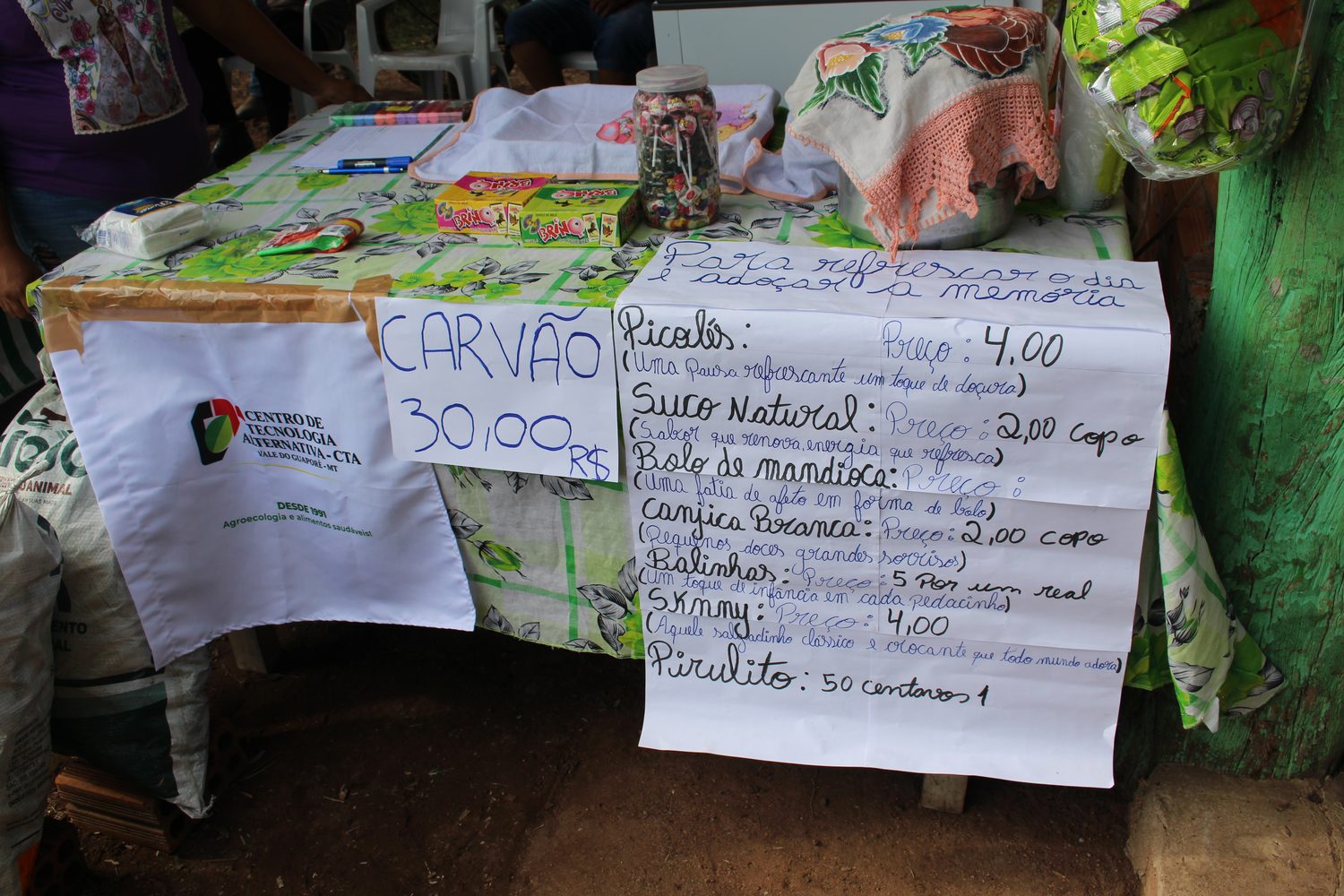 Cartaz com preços de picolé, suco natural, bolo de mandioca, canjica e carvão