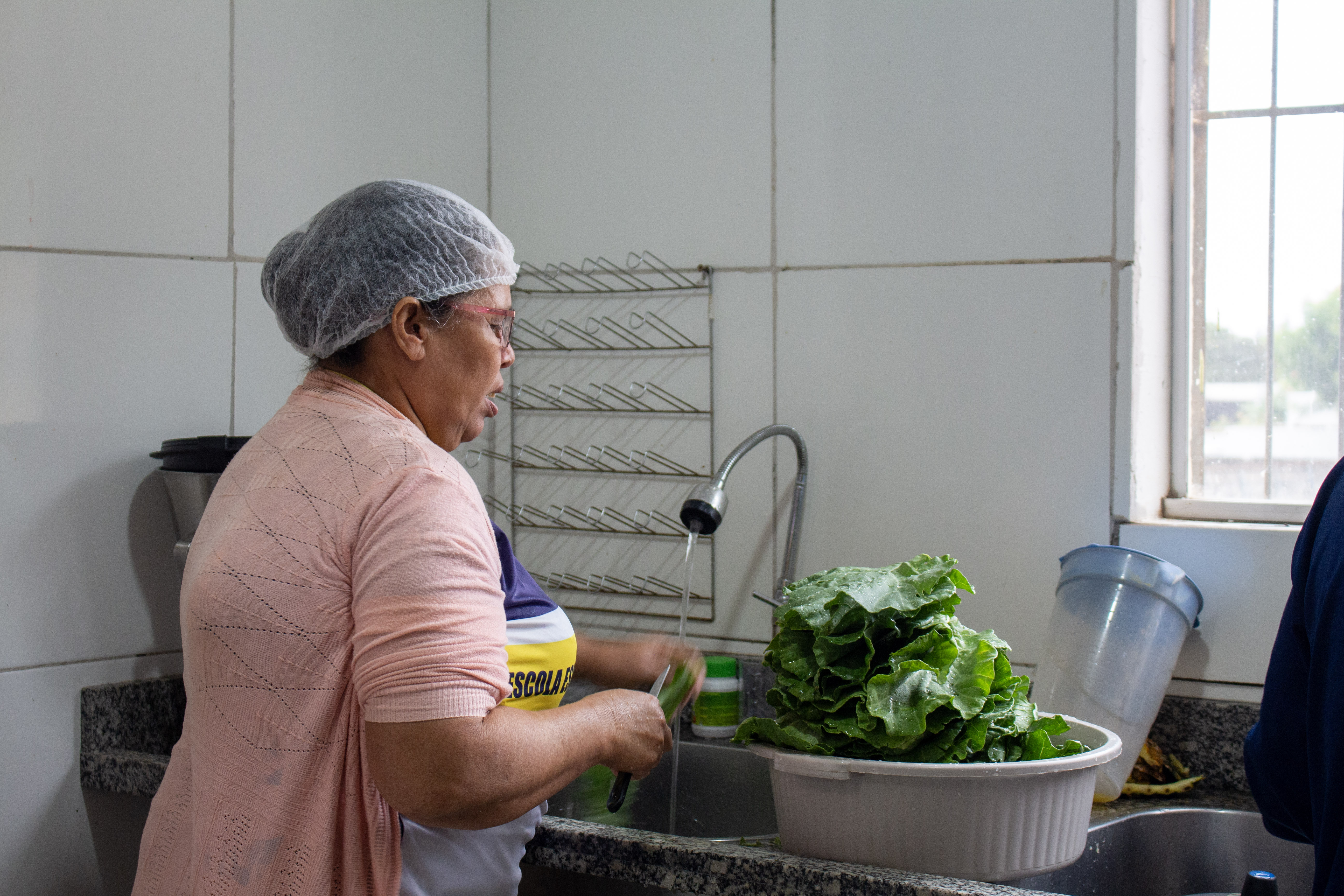Funcionária da APAE lavando alface na cozinha — verdura entregue pelo projeto PAA
