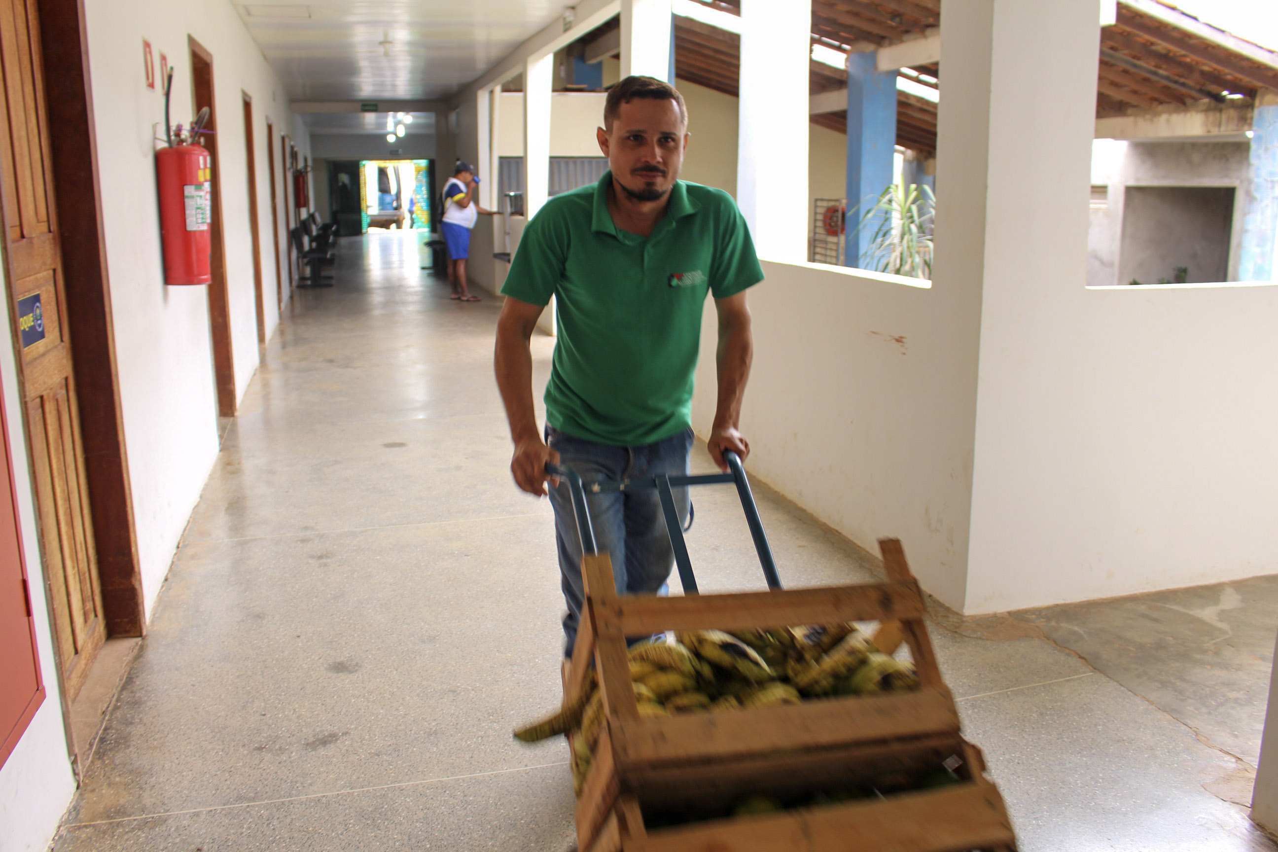 Técnico do CTA transportando caixote de banana pelo corredor da APAE