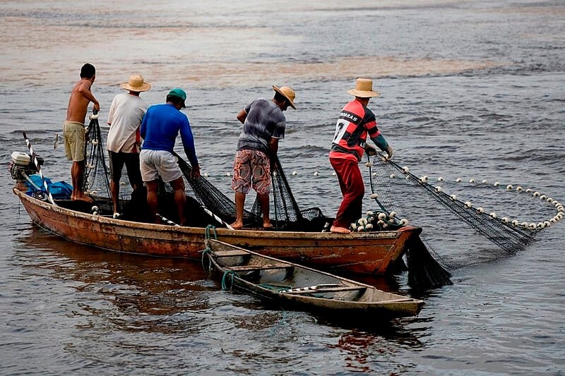 Pescadoras e pescadores artesanais puxando rede de barcos no rio